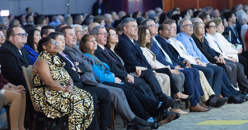 An audience is seated in a large event space.