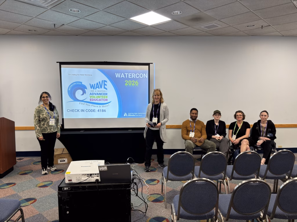 Two adults and four students pose for a photo in a conference room.
