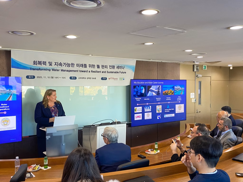 A woman stands at a podium in front of a classroom of attendees.