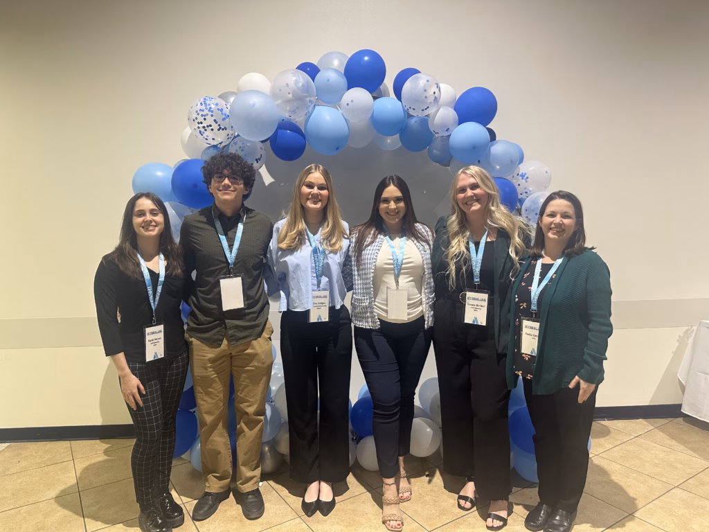 5 college students pose with their academic advisor at a networking event.