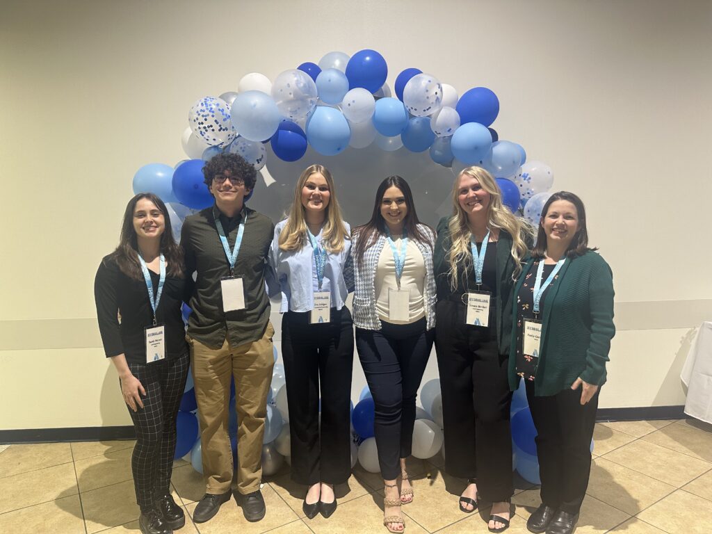 5 college students pose with their academic advisor at a networking event.