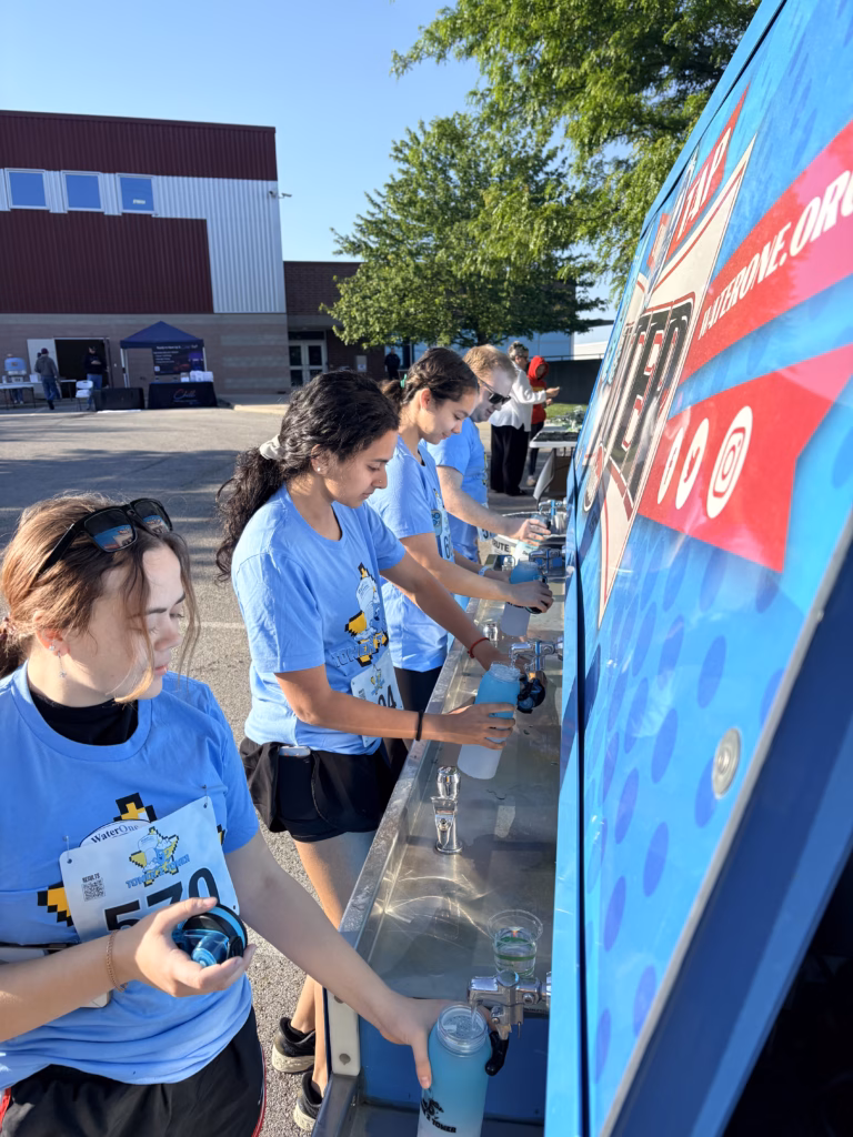 Young people fill water bottles at a mobile water station.