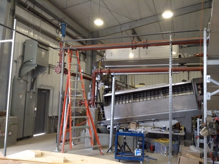 A dewatering screw press is being installed in a building at a sanitation district.